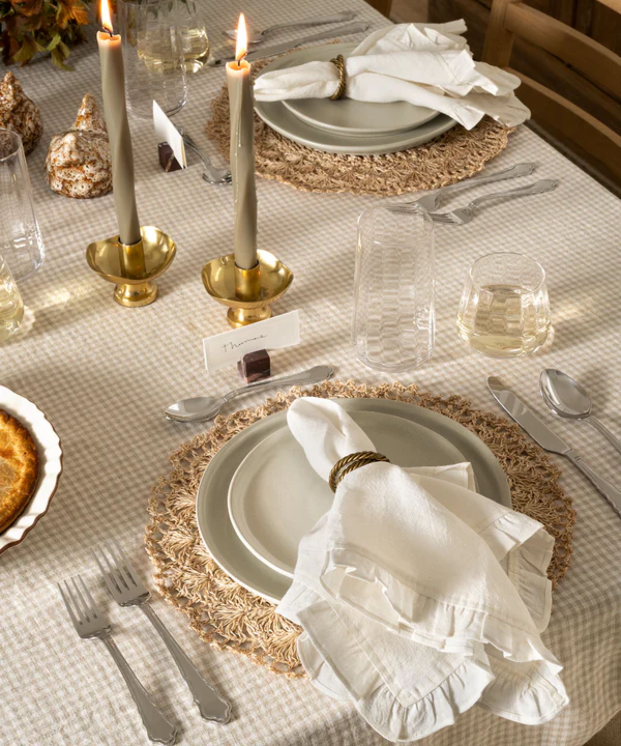 Cream and white gingham tablecloth with raffia placemats, white ruffle napkins, gold candle holders and sage green taper candles