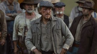 Jerome Flynn as Banner Creighton standing in front of a lot of people with his hands on his hips and looking to his right.