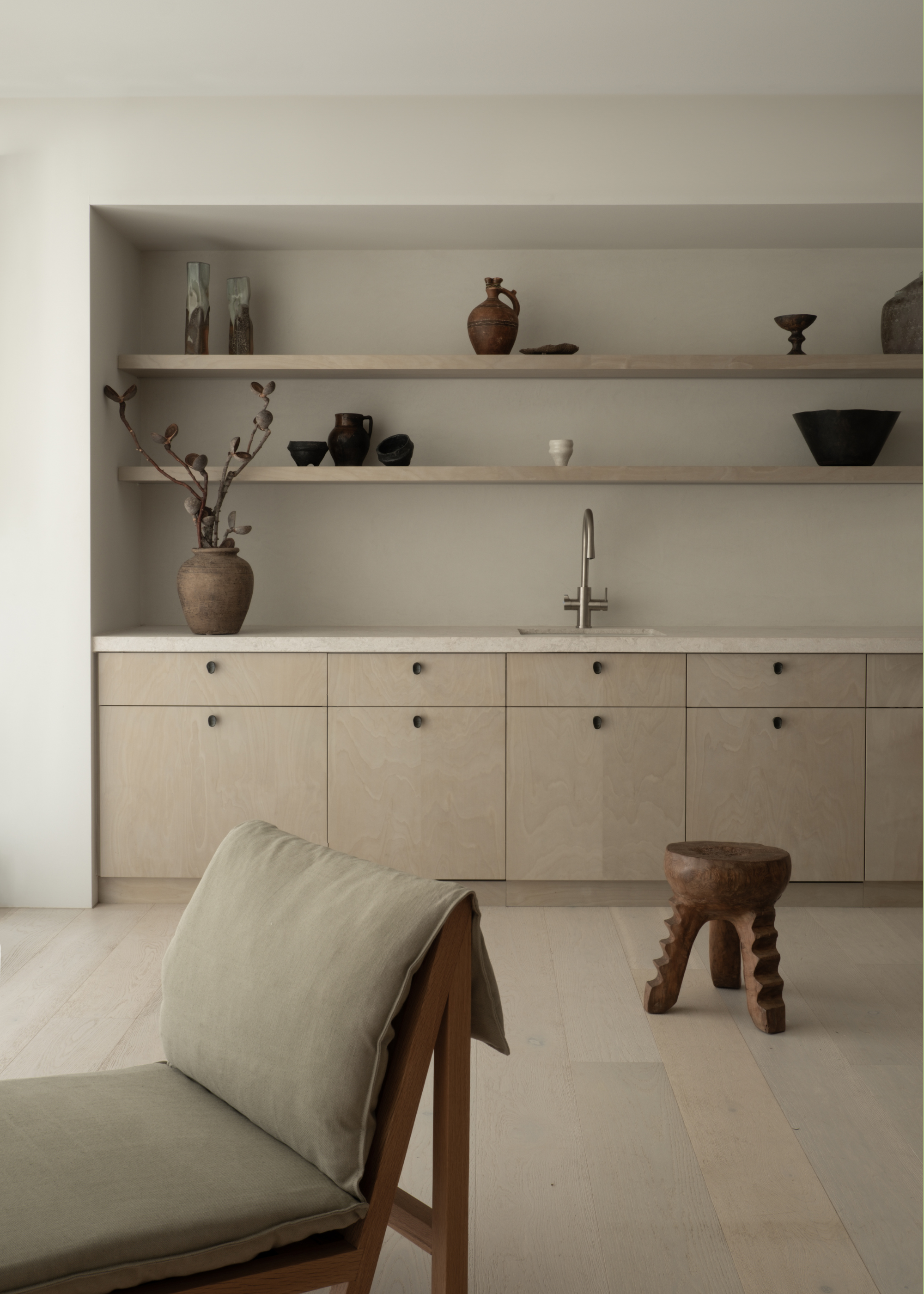 A living room with vases on wooden shelving, cabinets and a ridged wood stool near a sofa seater