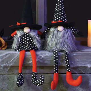 two halloween gonks sitting side by side, the one on the left in a black and white polka dot dress and shoes, orange leggings, and black hat with grey hair in pigtails, the one on the right with black and white polka dot outfit and hat, orange shoes and large grey beard