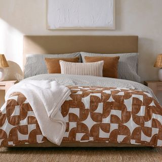 A bed with a patterned duvet cover with burnt orange abstract shapes and pin-striped cushions