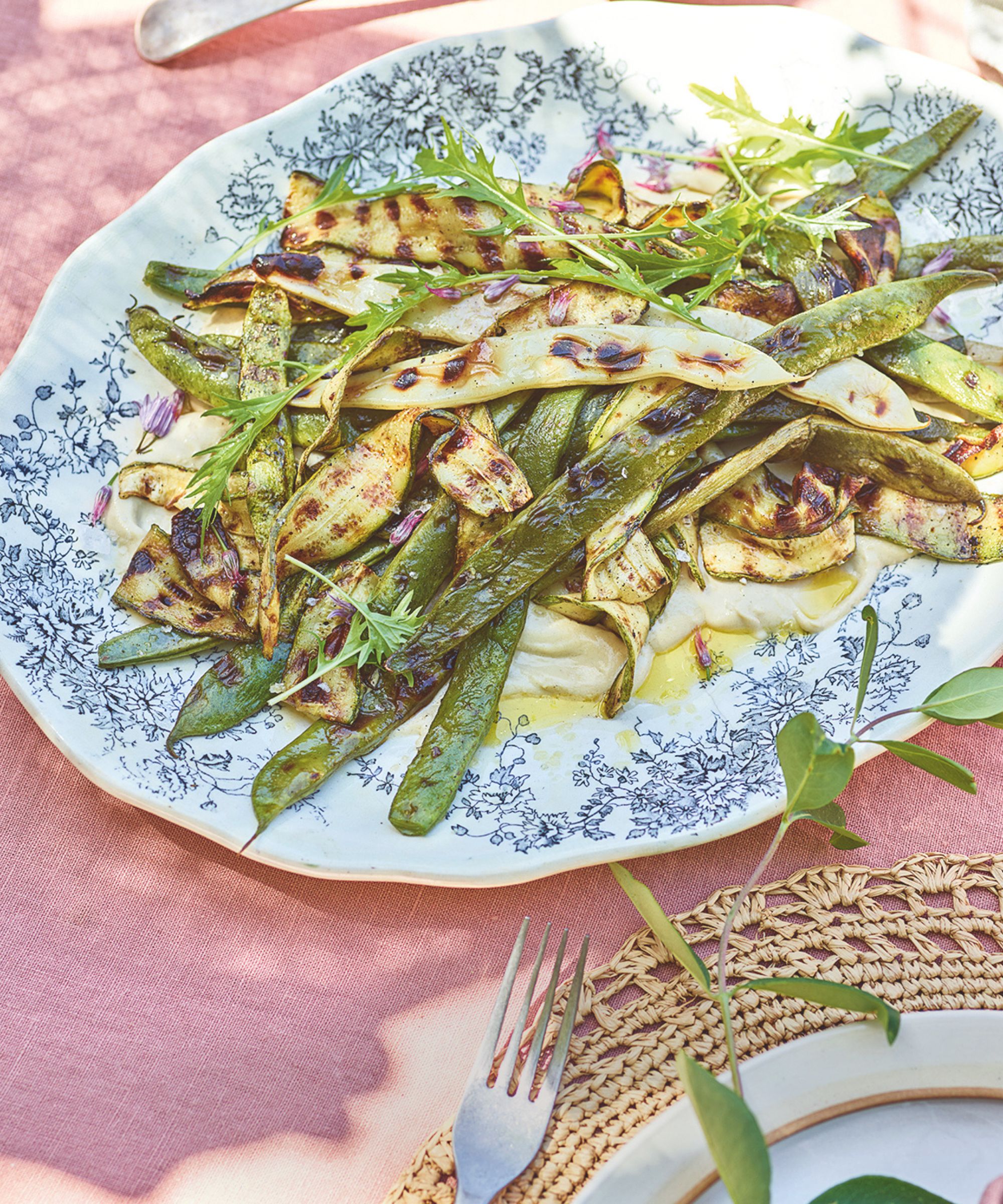 Platter of griddled courgette and beans on a pink tablecloth in the sunshine