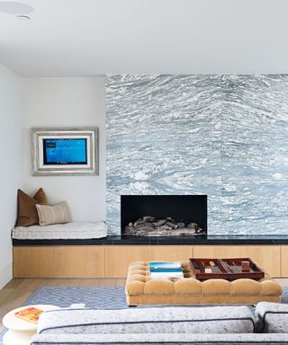 A water-effect wall with a built in fireplace and yellow foot rest, bench seating, wooden flooring.