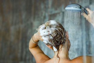 a woman with frizzy hair washing her hair in the shower