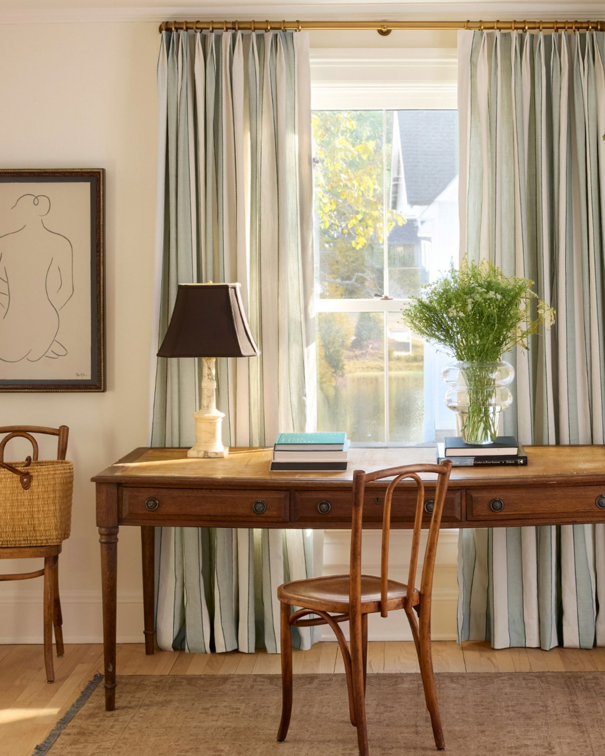 Image of sage green and cream stripped linen curtains in front of a window in an off-white room with wooden floors and antique furniture pieces. There is an antique writing desk and chairs.