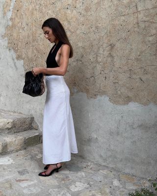 @iliridakrasniqi wearing a black halter top with a linen maxi skirt and black heeled sandals.