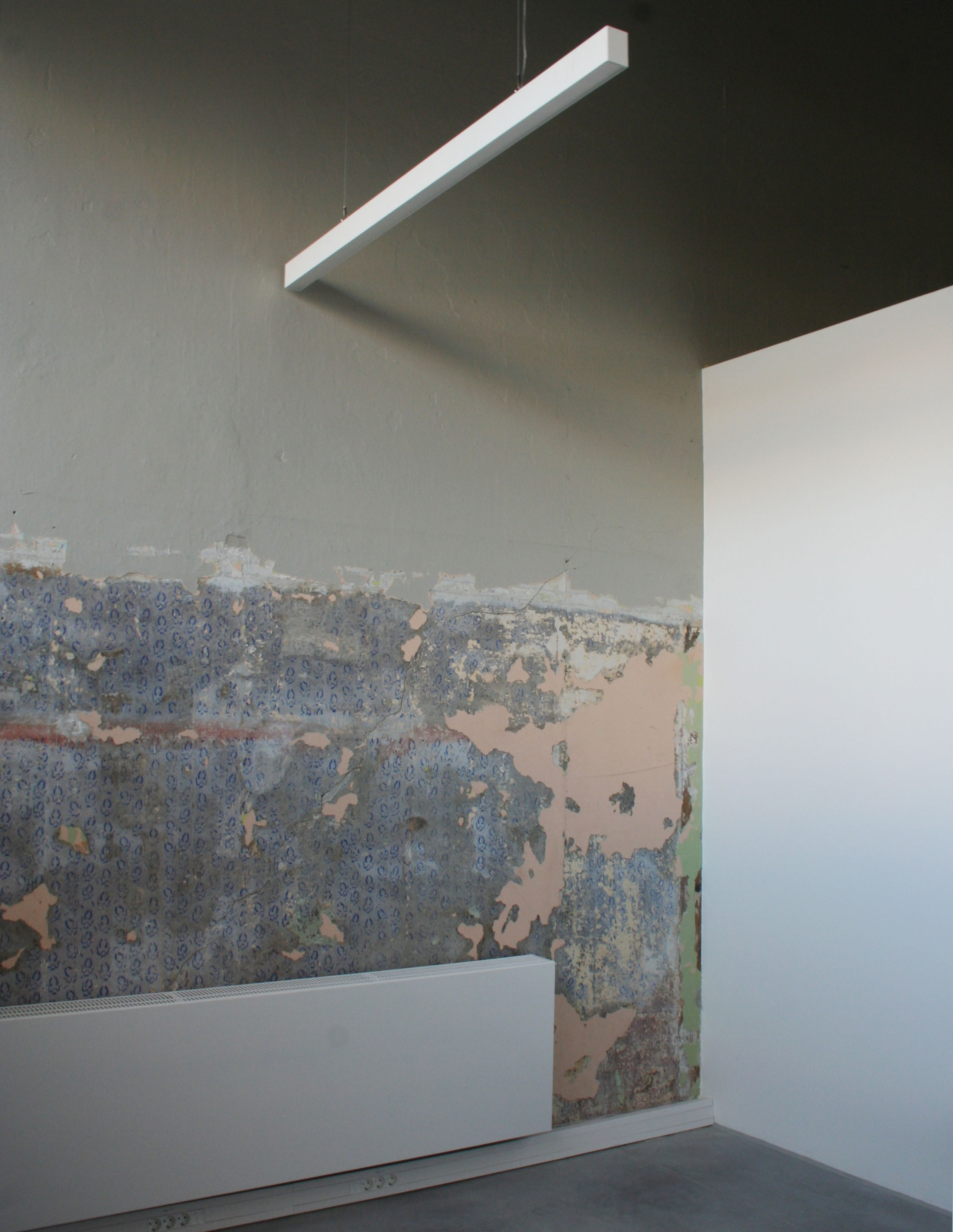 Interior showing a structural wall with layers of wallpaper from previous use.
