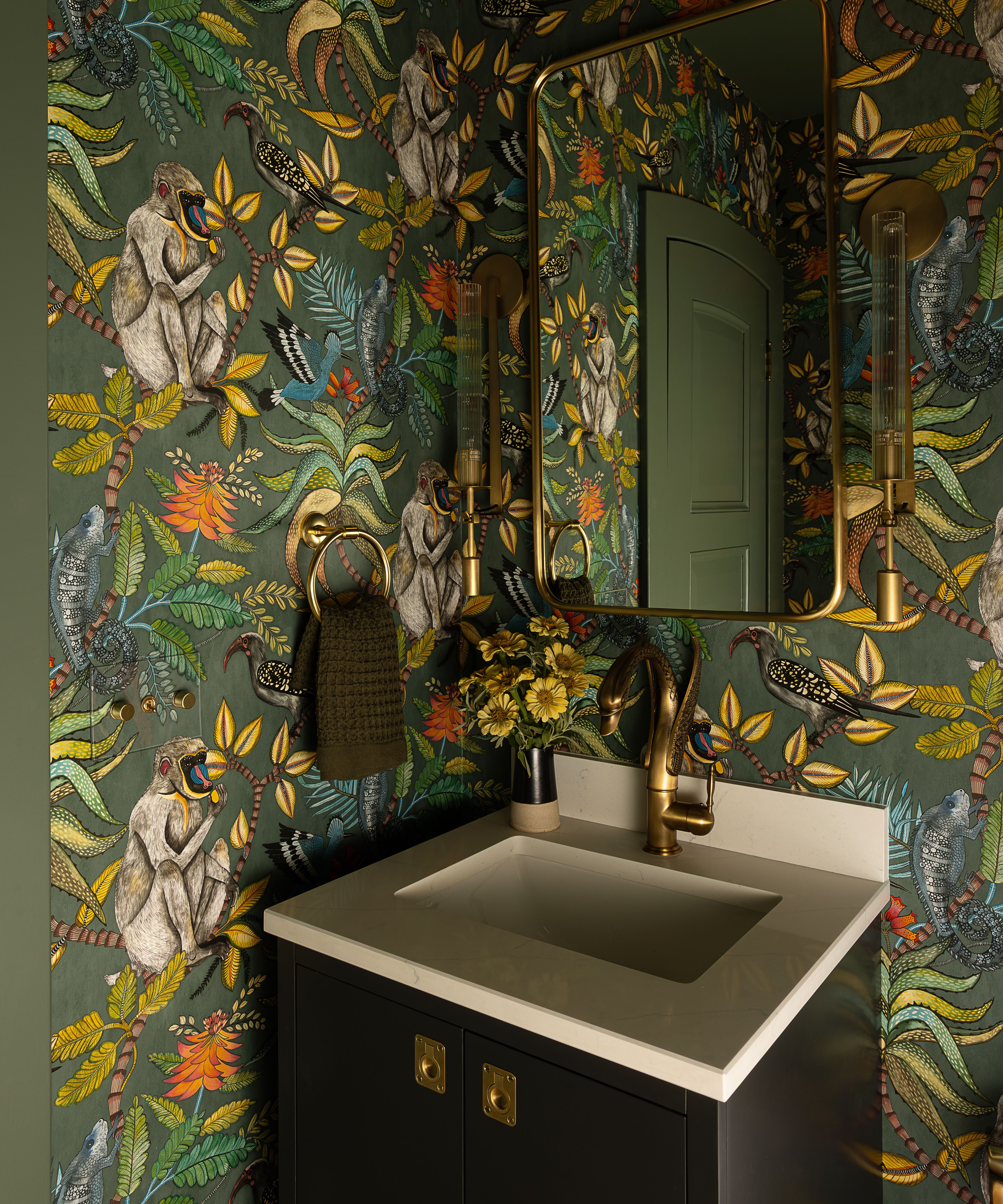 a small powder room wit vibrant green wallpaper with jungle and monkey themed motifs