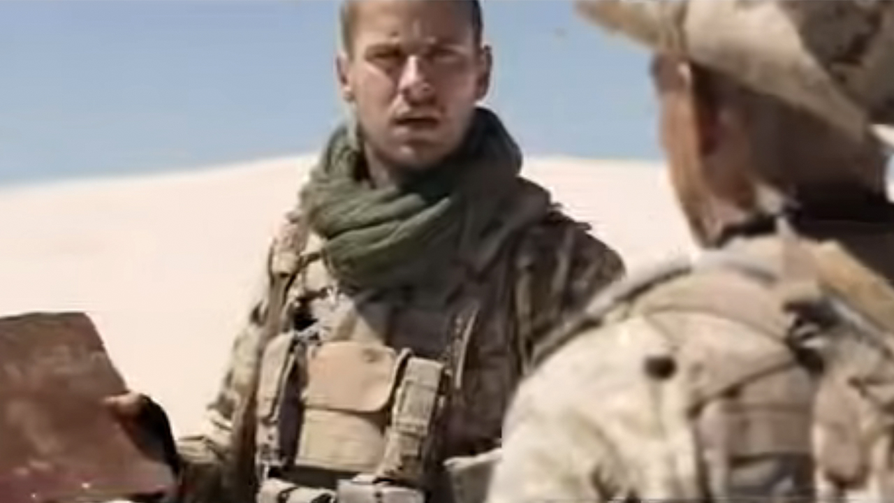 Two Marines looking at a piece of cardboard in the desert in Mine.