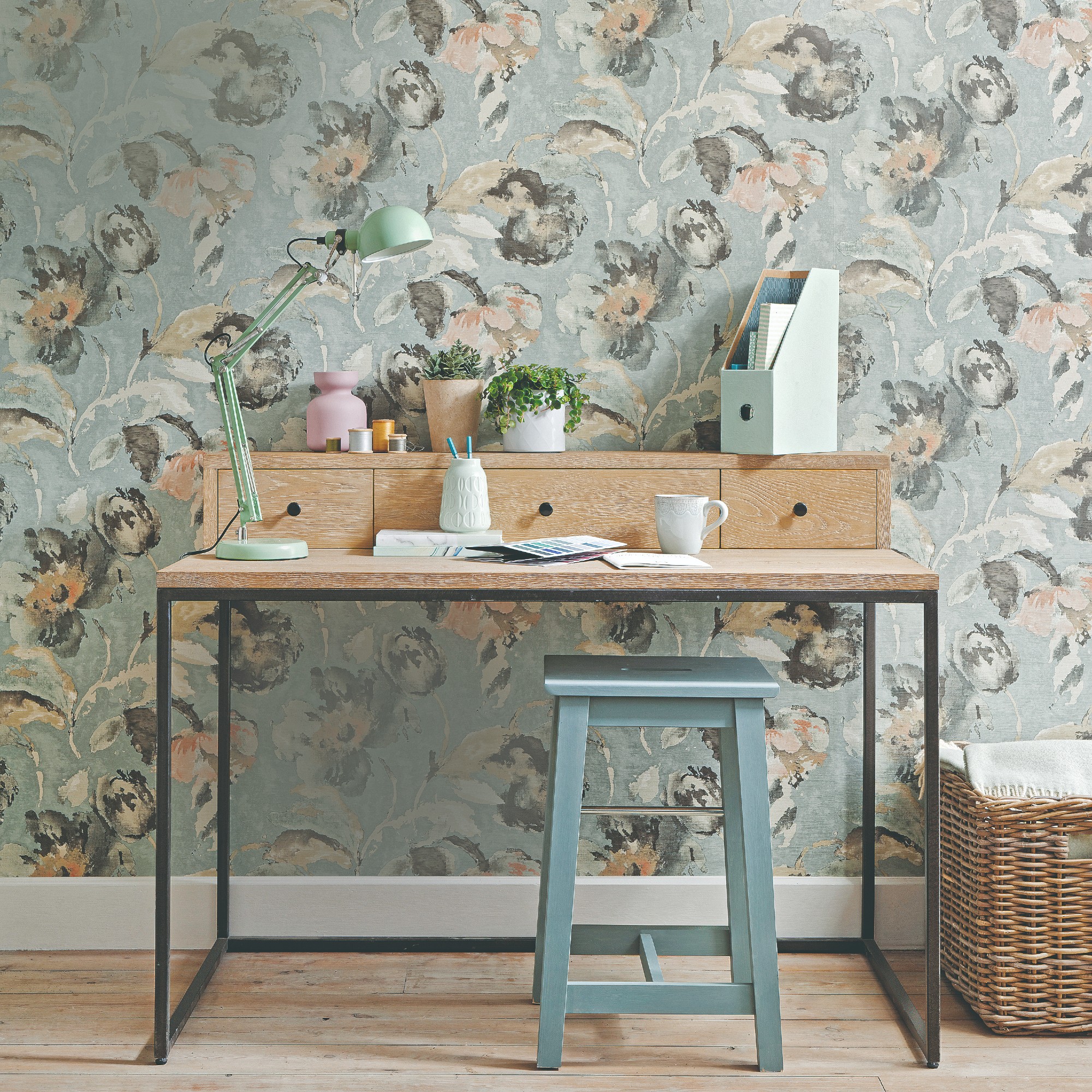 A home office set up with a desk, stool and a floral wallpaper