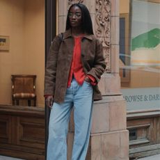 woman wearing a suede jacket, red knit top and light blue jeans