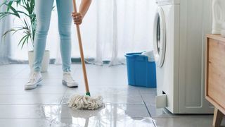 person mopping wet floor in front of washing machine