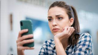 Close up of a depressed Caucasian young woman sitting at home, looking at her smartphone