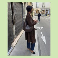 sylvie wears brown suede coat, jeans, black top, and deep brown leahter shoulder. bag