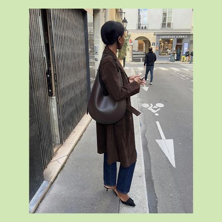 sylvie wears brown suede coat, jeans, black top, and deep brown leahter shoulder. bag