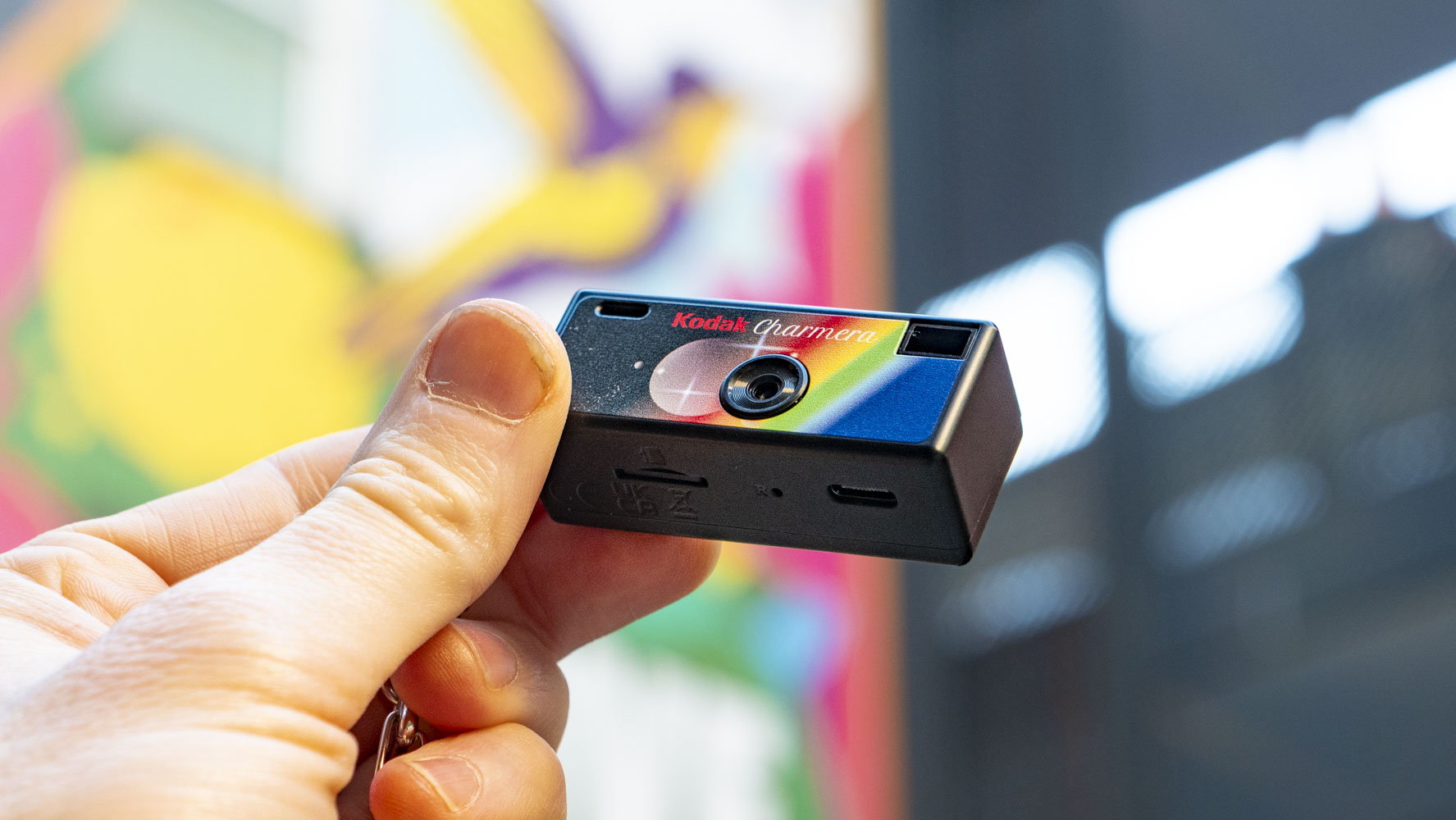 Kodak Charmera compact camera in user's hand with a vibrant graffitied wall backdrop