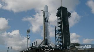 a black and white spacex falcon 9 rocket sits on the launch pad under a cloudy blue sky