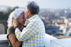 An older couple is embracing, and he is kissing the woman's forehead tenderly.