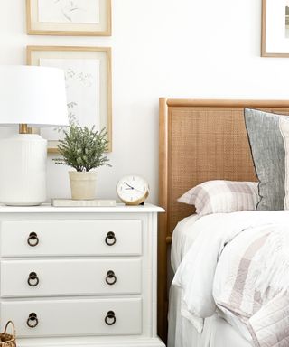 A white bedroom with wooden frames on the wall, a white dresser, and a jute bed with white bedding