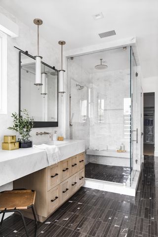 white bathroom with shower, shower bench, marble, black/grey floor tiles