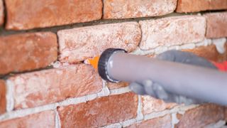 New grey mortar being fed into joints between red bricks with gun