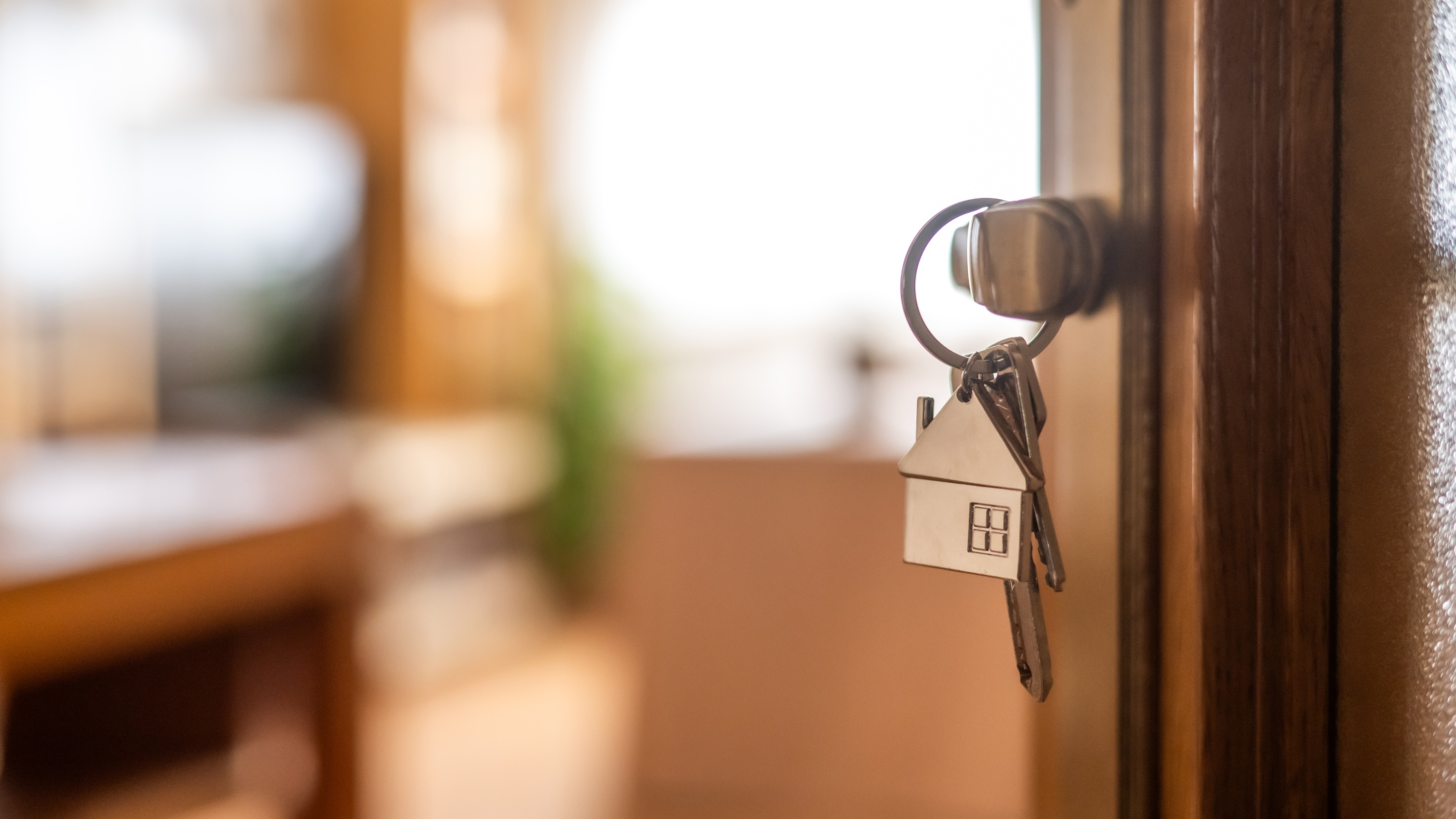 Keys with a home-shaped keychain draped over a door latch.