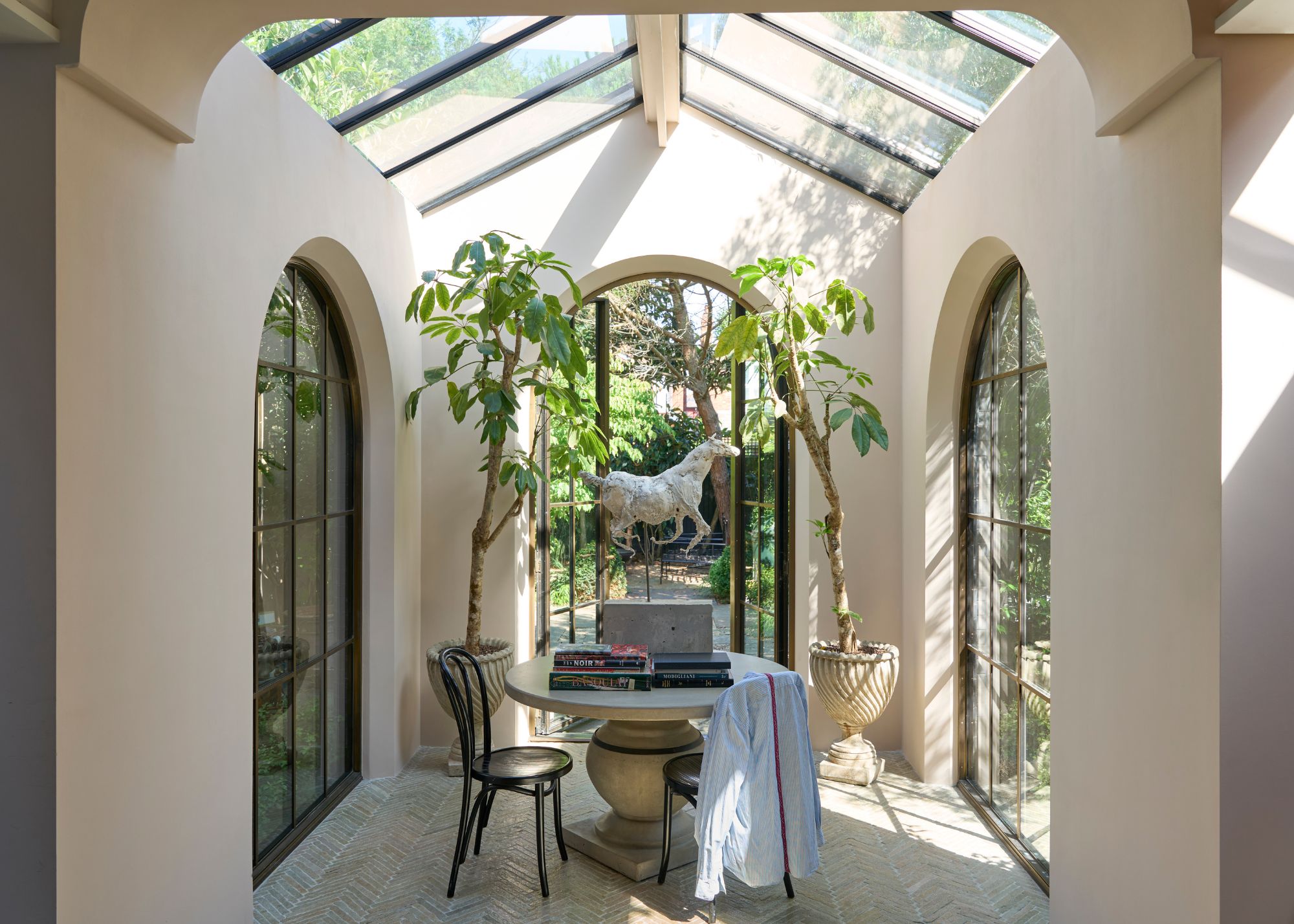 A light and airy conservatory room with soft neutral walls, three arched windows, and a sloped roof with skylights.