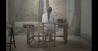 art installation of woman sitting at wooden desk