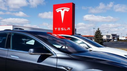 Tesla sedans in front of a Tesla sign