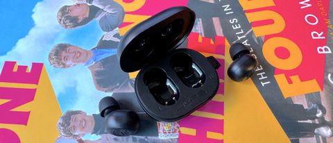 JLab JBuds Mini true wireless headphones on a book and technical mat, with hand and AirPods for comparison.