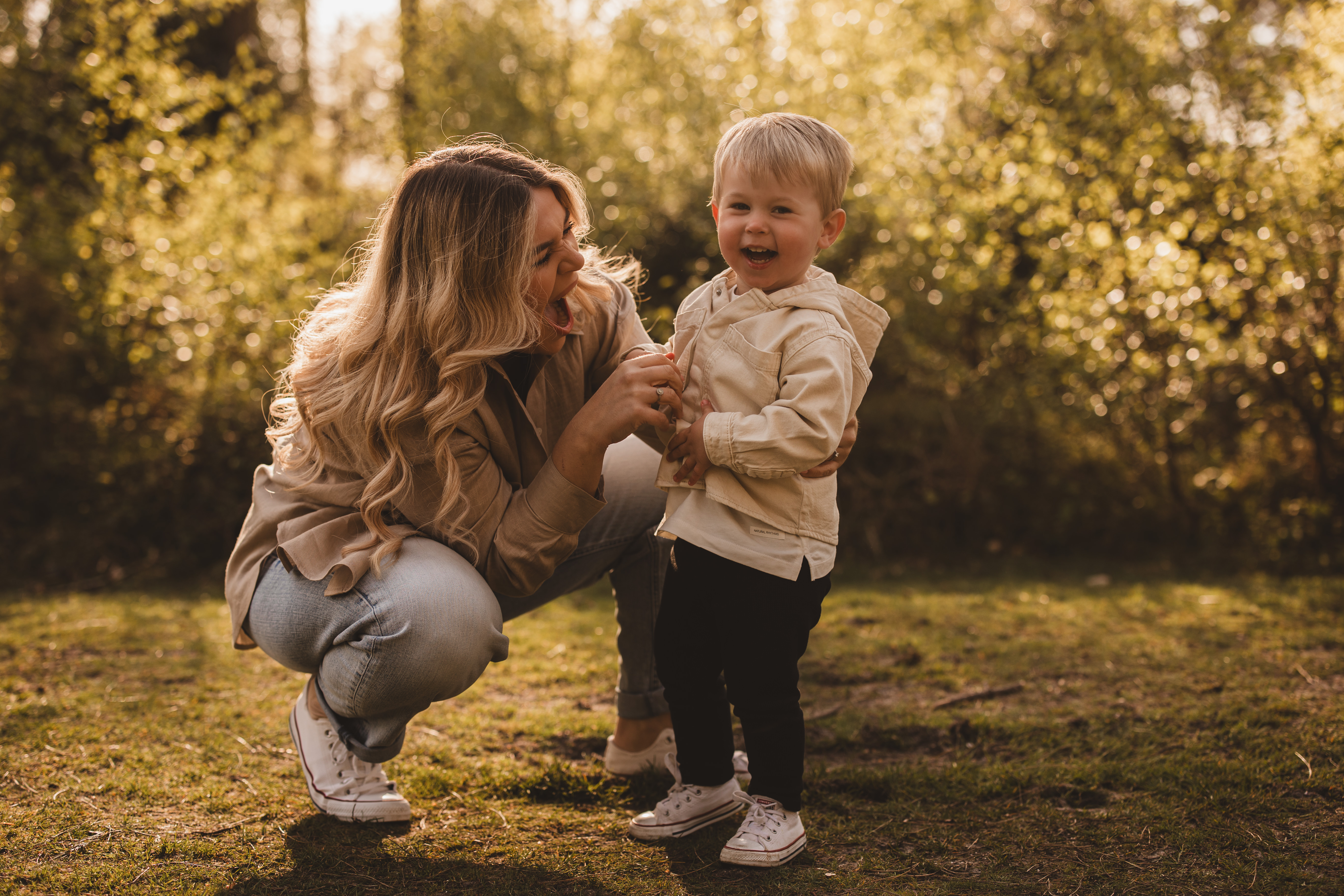 A mum and son crouch in a sunlit field laughing