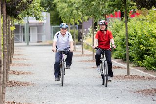 An older couple rides bicycles, wearing helmets.