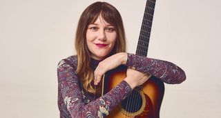 A portrait of Molly Tuttle wearing a patterned shirt, holding a Pre-War dreadnought