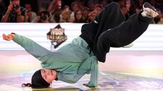 B-Girl Nicka Dominika breaking, in baggy black pants and a green fleece, ahead of the 2024 Paris Olympic Games.