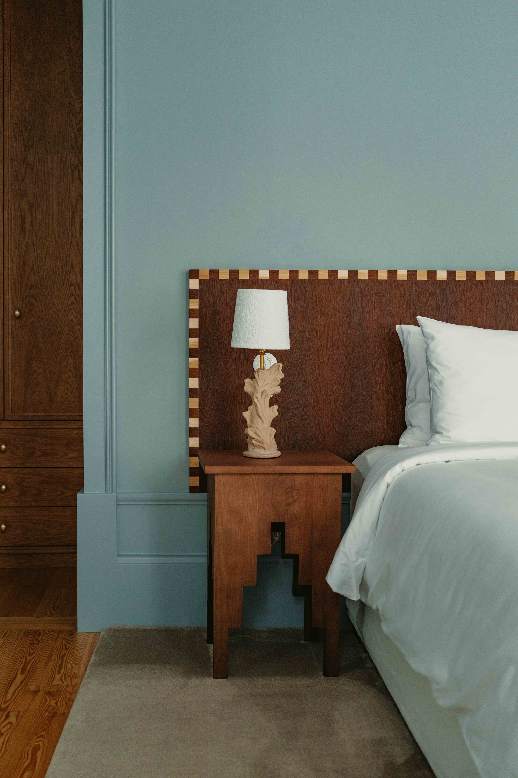 A bedroom with blue walls, a brown headboard with a checkered border, and a wooden nightstand