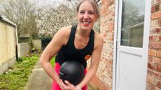 Maddy Biddulph stands outside in her backyard, holding a medicine ball in her hands and smiling at the camera.