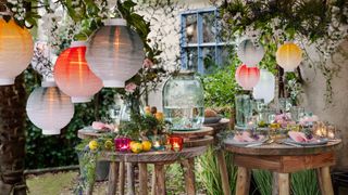 decorating for a garden party with paper lanterns hanging from trees above dining tables