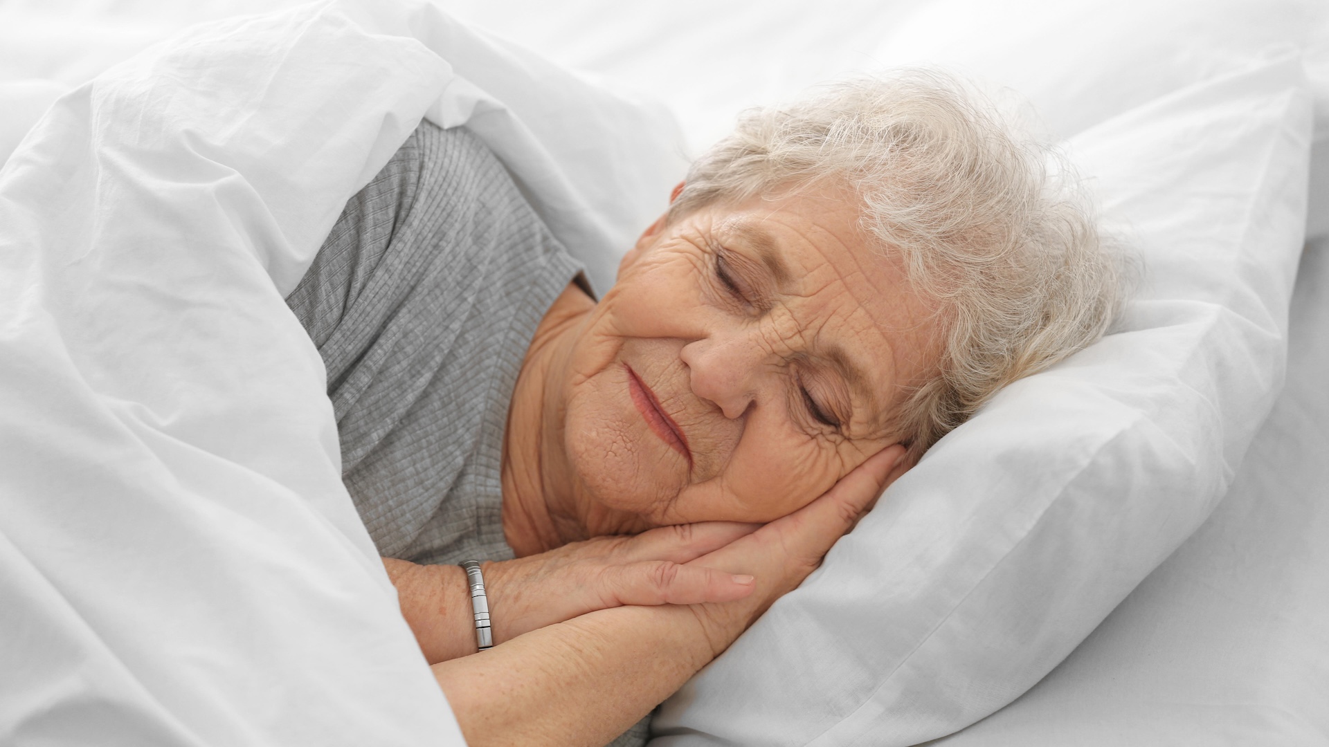 An older woman asleep in bed under a white comforter