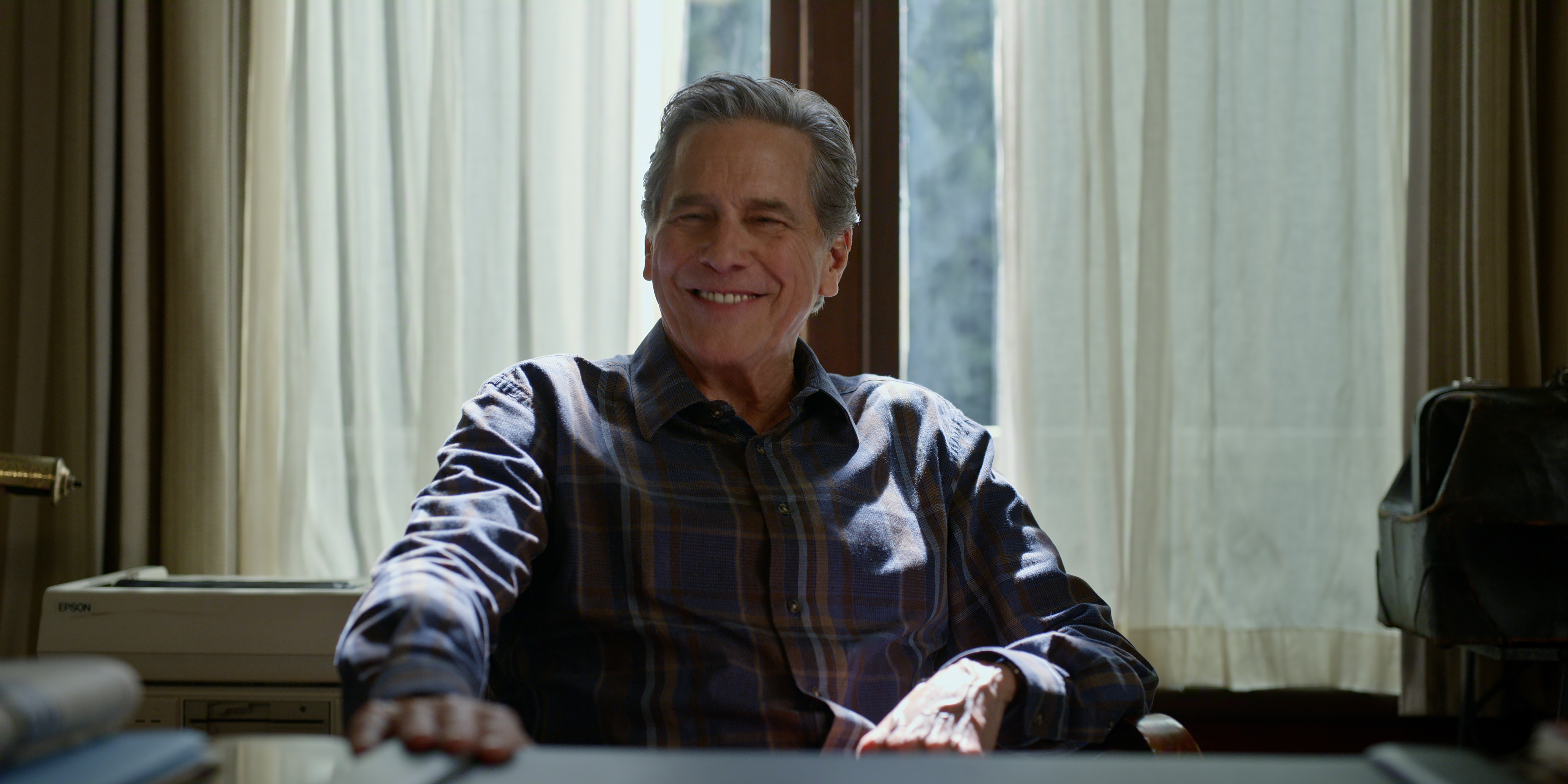 Tim Matheson as Dr. Vernon Mullins in Episode #708 of Virgin River smiling and sitting at a desk wearing a button down