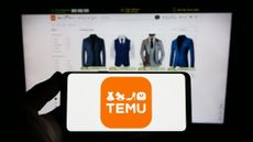 Person holding smartphone with logo of US online shop company Temu on screen in front of website