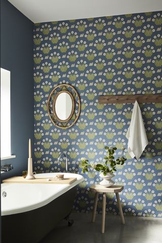 A blue bathroom with green and blue wallpaper with a rattan mirror and a peg rail