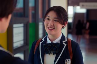 Audrey Huynh as Stella smiling and wearing a school uniform in the kiss hallway in in episode 207 of XO, Kitty.