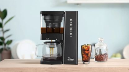 Shine Rapid Cold Brew Coffee Maker on a countertop with a cup of coffee at the side