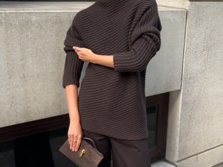 Woman wears a chocolate brown ribbed Toteme sweater with COS trousers and white Manolo Blahnik Maysale slingbacks.