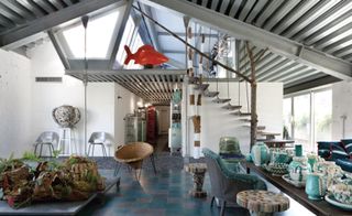 A room with different shaped chairs, different shaped pots, plants growing out of tree stumps, shelving trolleys and a staircase.