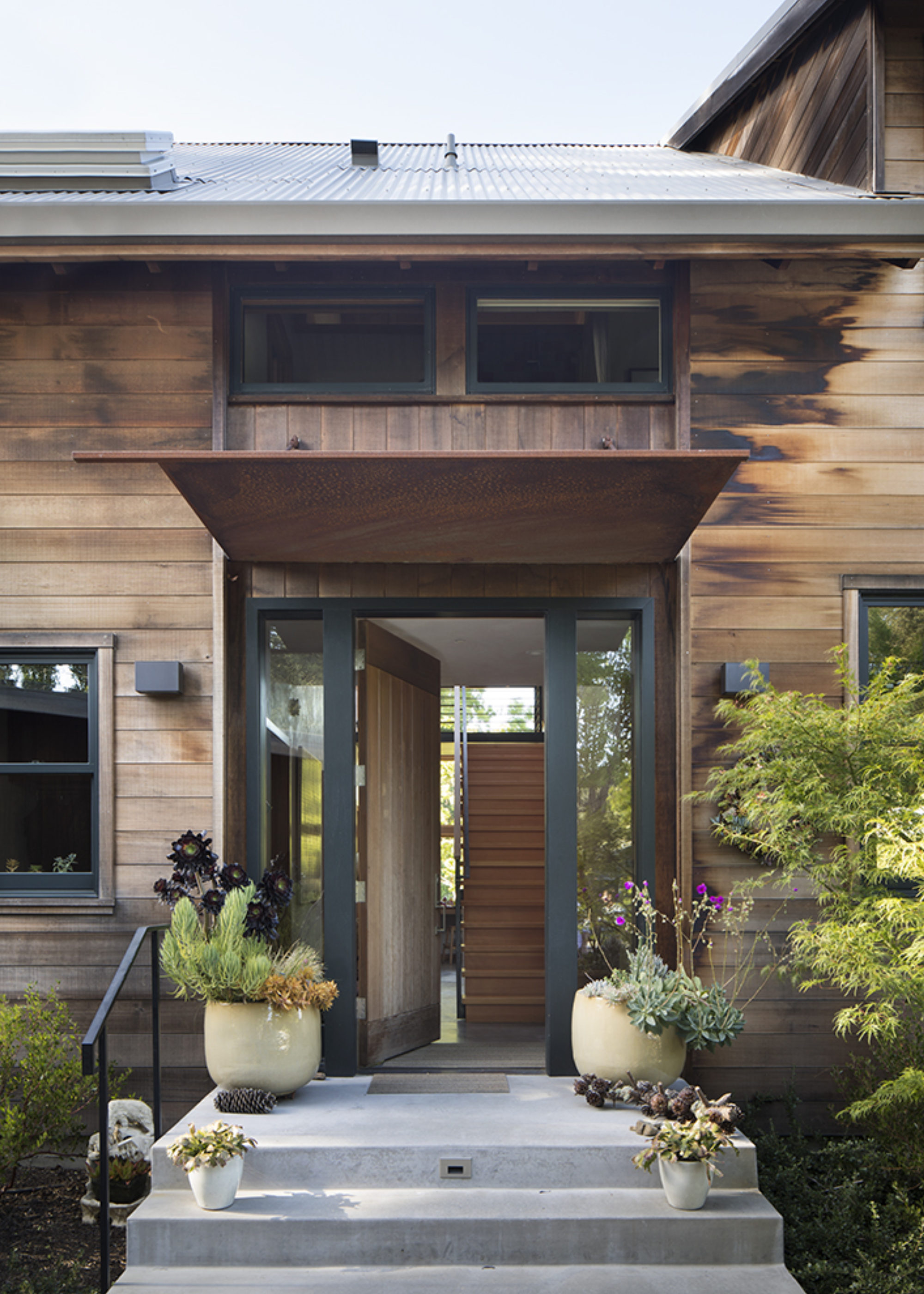 A front door of a timber clad house with potted plants on concrete steps