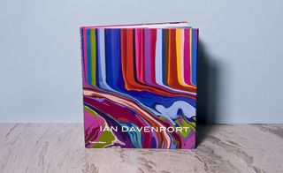 Ian Davenport Book. A book standing on a wooden surface with many colourful vertical lines smudging together on the lower half of the cover.
