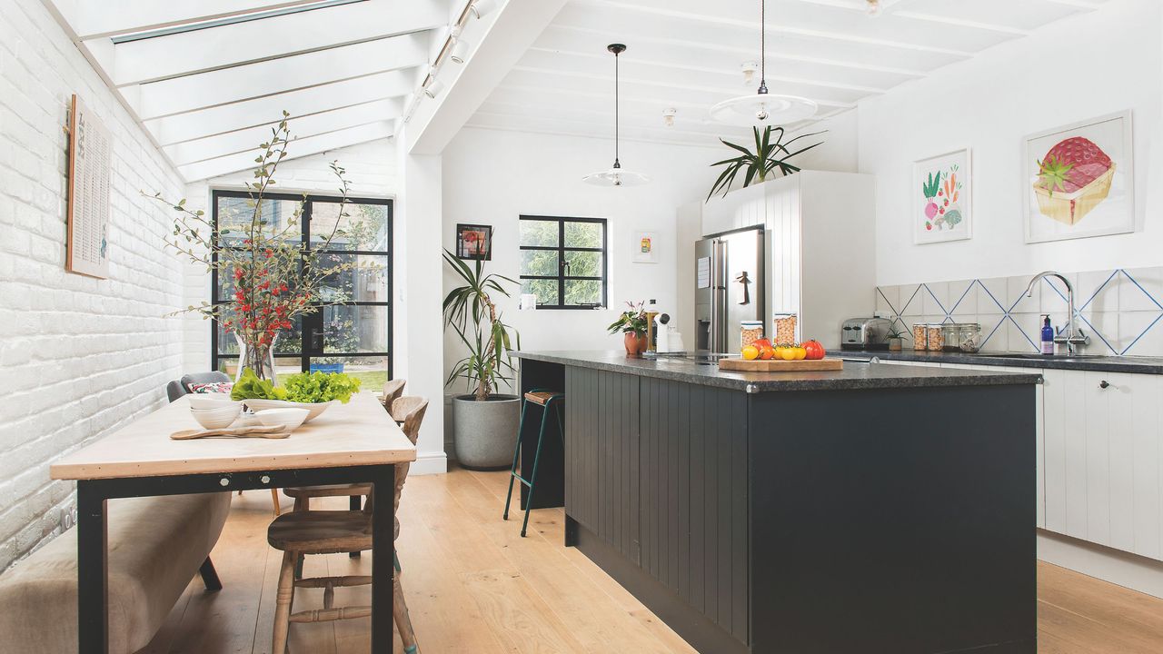 Side return kitchen extension with white walls, wood flooring, black kitchen island and fixed rooflights overhead