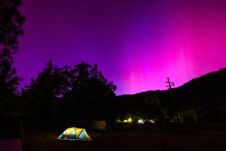 pink and purple northern lights over a tent that's lit from within in a campground
