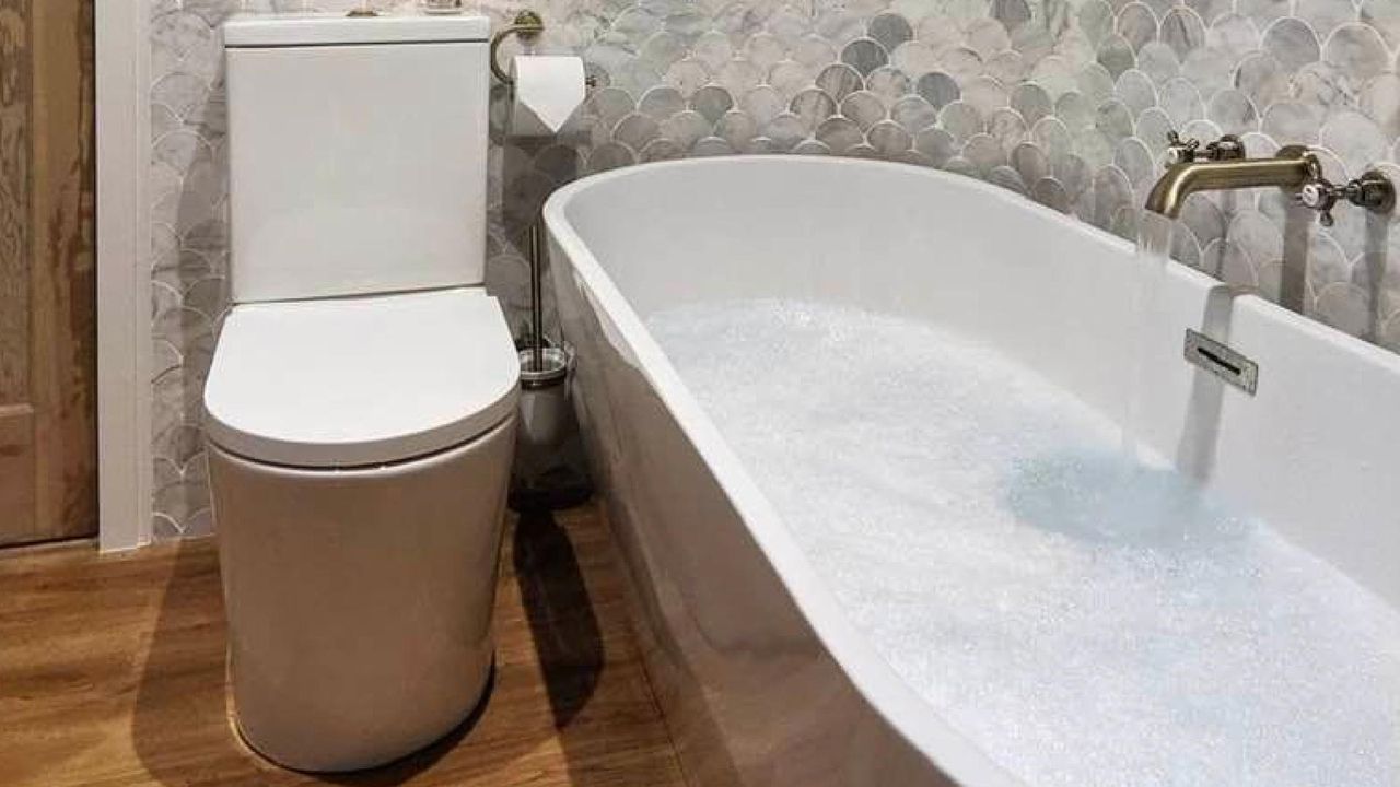 bathroom with white bath and toilet with grey wall tiles